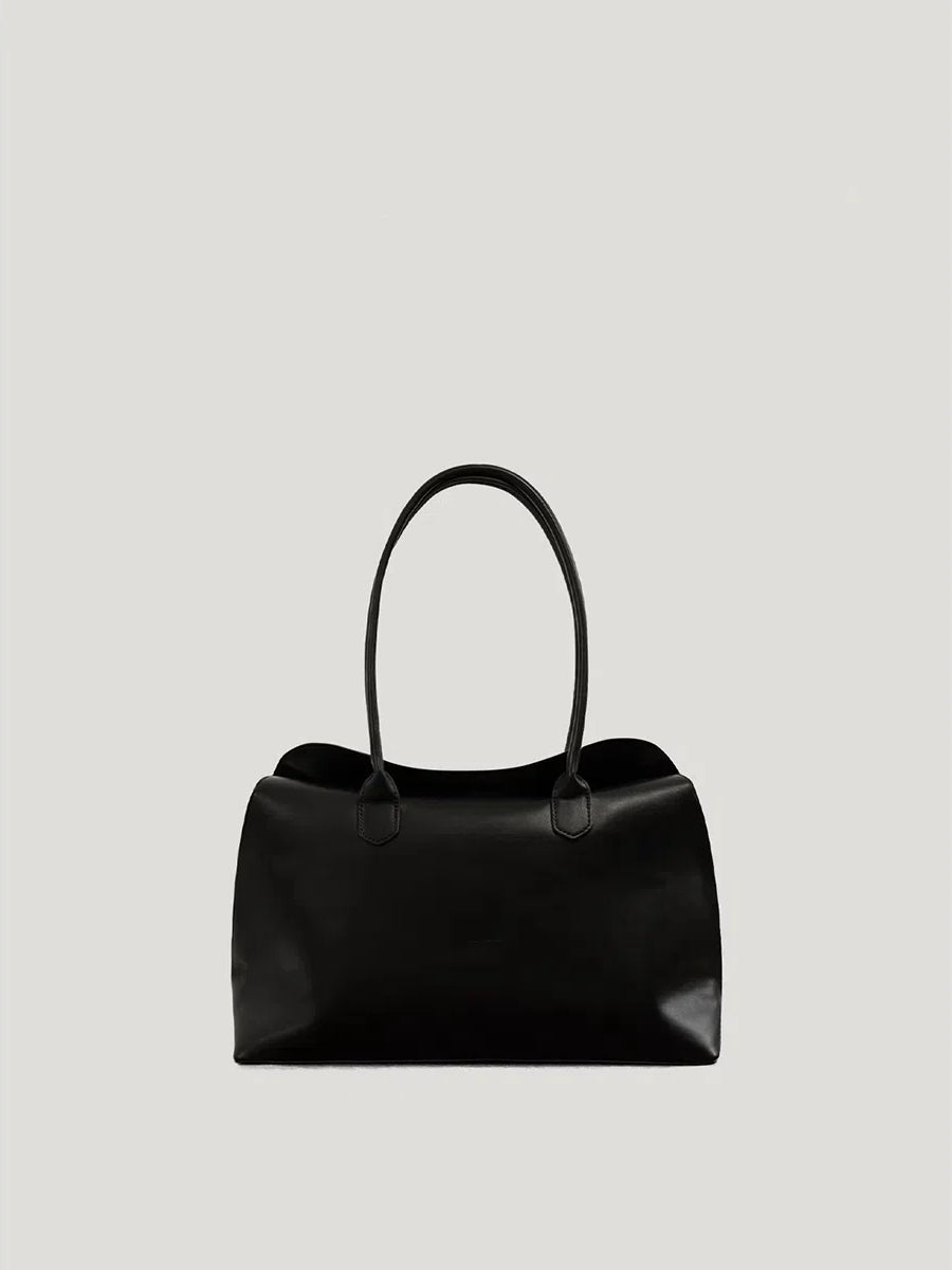 A large black leather bag with a spacious top handle design, shown from the front on a light gray background.