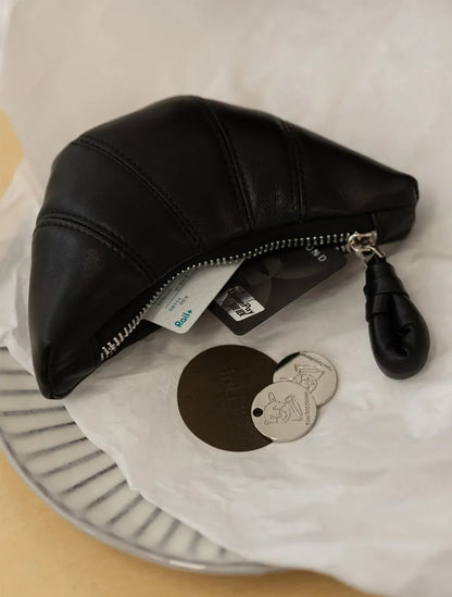 A black leather purse with credit cards stuffed inside lies flat on a white paper atop a plate, next to coins.