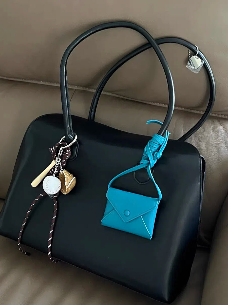 An envelope-shaped blue crossbody wallet, made from real leather, with its strap tied to the handle of a black leather bag.