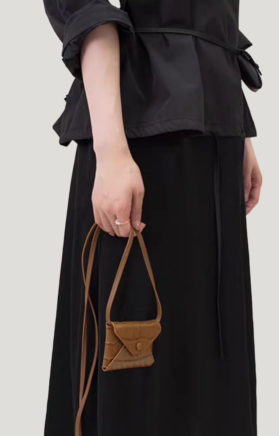 A model holds the strap of an envelope-shaped brown crossbody wallet, made from real leather with a crocodile skin pattern.