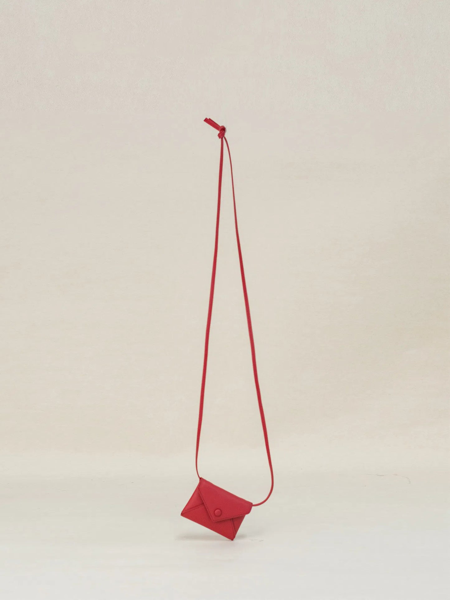 An envelope-shaped red crossbody wallet, made from real leather and featuring a long strap, hangs against a white background.